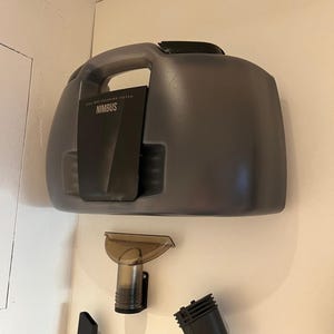 Könnte beinhalten: Ein graues Nassreinigungssystem mit dem Aufdruck "NIMBUS" auf der Vorderseite. Das System hat einen Griff und ist an einer Wand befestigt. Mehrere Aufsätze sind darunter zu sehen, darunter eine Bürste und verschiedene Düsen.