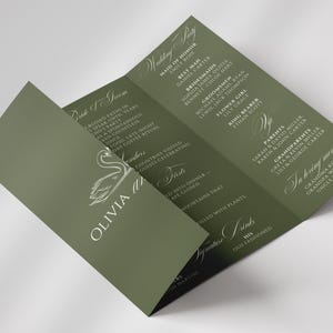 May include: An olive green tri-fold wedding invitation. The invitation has white script and a swan illustration. The text includes the wedding party, parents, and grandparents' names. The invitation is open, displaying the details of the event.