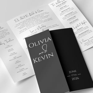 Könnte beinhalten: Eine Hochzeitseinladung mit einem dreifachen Design und einem dunkelgrauen Umschlag. Der Umschlag zeigt die Namen "Olivia und Kevin" in weißer Schrift, darunter das Datum "17. Juni 2026". Zusätzliche Tafeln detaillieren die Hochzeitsinformationen.