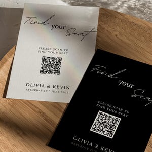 以下が含まれることがあります： 2つのウェディング席札。白と黒があり、エレガントな筆記体で「Find your Seat」と書かれています。各カードにはQRコードと「Olivia & Kevin」の名前、日付「Saturday 17th June 2025」が記載されています。