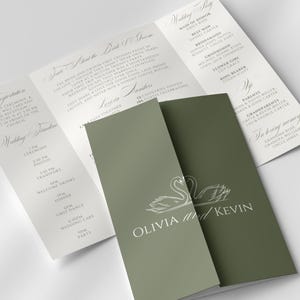 Op de afbeelding: Trouwkaart in saliegroen met een zwanenontwerp en de namen Olivia en Kevin. De open uitnodiging onthult details over de ceremonie, receptie en bruiloftsgasten. Elegant en klassiek ontwerp.