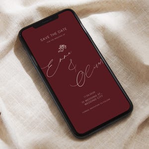 May include: A smartphone screen shows a digital wedding invitation in burgundy. The text reads "Save the Date" and features the names "Emma & Oliver" in elegant script. The date is 17 June 2026, with a location and "Formal Invitation to Follow."