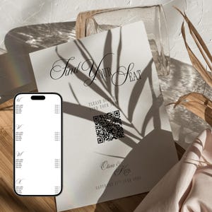 以下が含まれることがあります： Find Your Seatという黒い文字、QRコード、Olivia & Kevinという名前、そしてSaturday 17th June 2026という日付が記載された白い結婚式の座席表サイン。印刷されたサインの横には、デジタルゲストリストを表示したスマートフォンが置かれています。