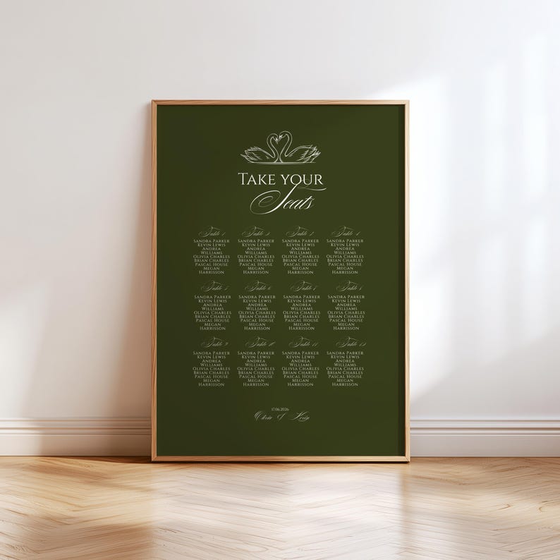 May include: A framed seating chart with a dark green background. The chart features elegant white text, including the words "Take Your Seats" and guest names. Two swans are at the top. The frame is gold.