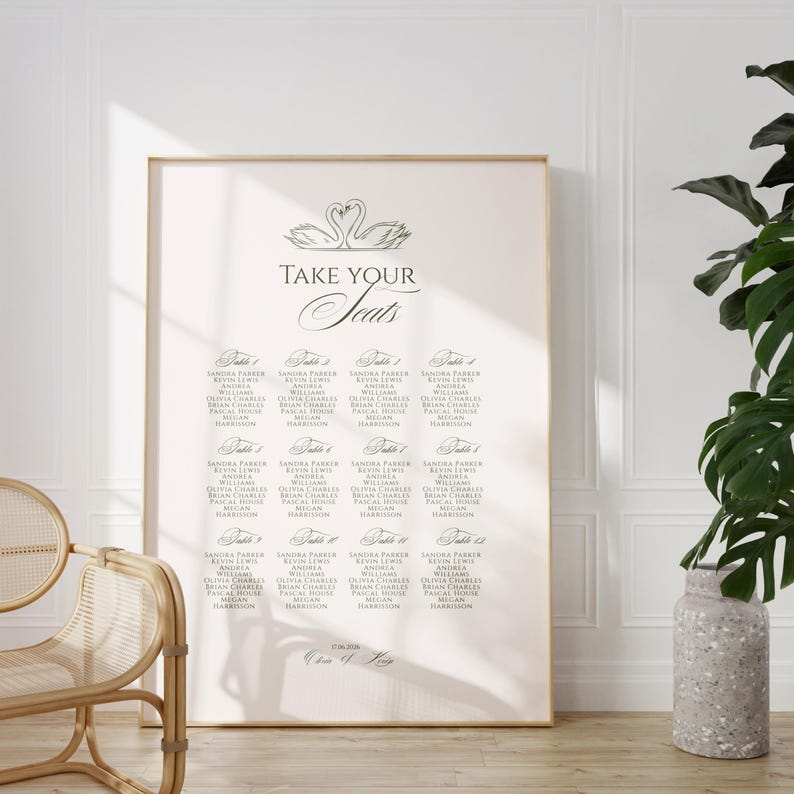 May include: A large, framed seating chart with the words "TAKE YOUR Seats" in elegant script. The chart lists names under table numbers, with a swan illustration at the top. The overall color scheme is neutral, with a light background and dark text.