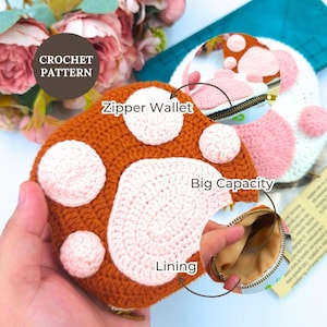 May include: A brown and pink crochet zipper wallet shaped like an animal paw with a beige interior lining. The wallet features a large central pad and four smaller circular pads in light pink. Text on the image reads CROCHET PATTERN, Zipper Wallet, Big Capacity, and Lining.