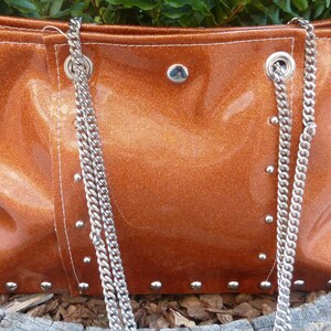 May include: A brown leather tote bag with a silver chain strap and silver studs. The bag has a shiny, metallic finish.