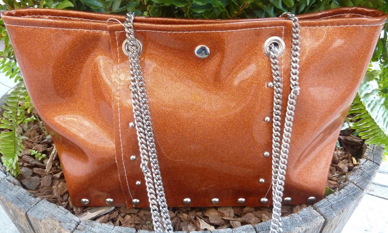 May include: A brown leather tote bag with a silver chain strap and silver studs. The bag has a shiny, metallic finish.