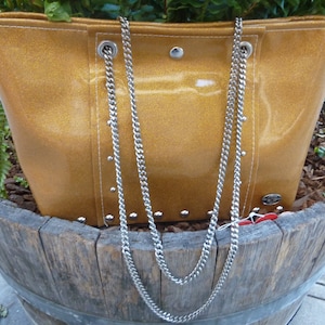May include: A gold glitter tote bag with a silver chain strap. The bag has silver studs around the edges and a white stitch detail.