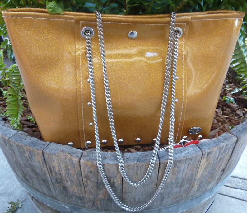May include: A gold glitter tote bag with a silver chain strap. The bag has silver studs around the edges and a white stitch detail.