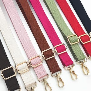 May include: Eight colourful purse straps in a range of shades, including black, white, pink, brown, fuchsia, green, red, and navy. Each strap has gold-coloured metal hardware, including adjustable buckles and swivel clasps for easy attachment.