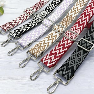 Puede incluir: Surtido de correas de bolso coloridas con patrones geométricos. Las correas presentan varios colores, incluyendo burdeos, negro, lavanda, marrón claro, rojo y negro y gris. Cada correa tiene herrajes metálicos plateados, incluyendo hebillas ajustables y cierres giratorios.