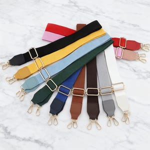 以下が含まれることがあります： 赤、黒、黄色、青、緑、茶色、グレー、白など、さまざまな色合いのカラフルな交換用バッグストラップのコレクション。各ストラップには、調節可能なバックルや回転式クラスプなど、金色の金属製ハードウェアが備わっています。