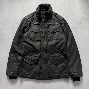 May include: A black jacket with a high collar and multiple front pockets. The jacket has a rugged, worn appearance, with a slightly shiny finish. The sleeves have ribbed cuffs, and the jacket appears to be made of a durable material.