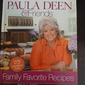 May include: A cookbook titled "PAULA DEEN & Friends" features a smiling woman in an orange shirt. The book cover includes the text "Family Favorite Recipes" and a "Living It Up Southern Style!" sticker.