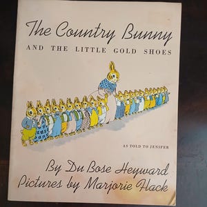 May include: Vintage children's book cover titled "The Country Bunny and the Little Gold Shoes." The cover features an illustration of a bunny leading a line of bunnies, all dressed in colorful outfits. The author and illustrator's names are also displayed.