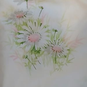May include: A floral pattern featuring white daisies with pink centers and green stems and leaves. The design is set against a soft, off-white background, creating a delicate and airy aesthetic. The artwork has a watercolor-like quality.