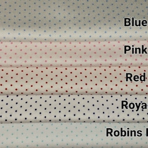 Op de afbeelding: Vijf stofstalen met een witte achtergrond en verschillende gekleurde stippen. De stalen zijn gelabeld met "Blauw", "Roze", "Rood", "Koninklijk" en "Robijnrood".
