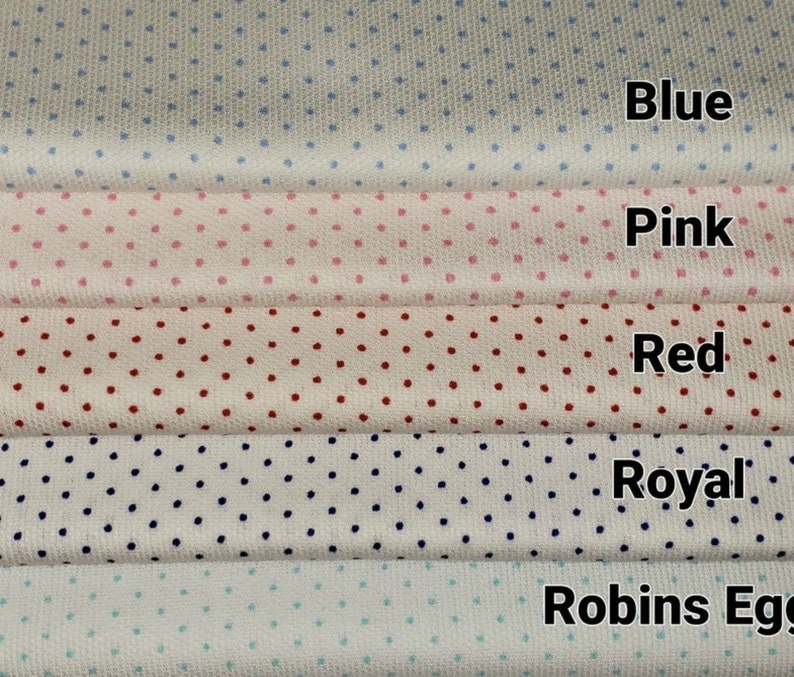 Op de afbeelding: Vijf stofstalen met een witte achtergrond en verschillende gekleurde stippen. De stalen zijn gelabeld met "Blauw", "Roze", "Rood", "Koninklijk" en "Robijnrood".
