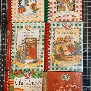 May include: A collection of Gooseberry Patch cookbooks with spiral bindings. Titles include "Welcome Home For The Holidays", "Old-Fashioned Country Christmas", "Coming Home for Christmas", "Christmas Pantry", "Christmas with Family & Friends", and "Fall Family & Friends".