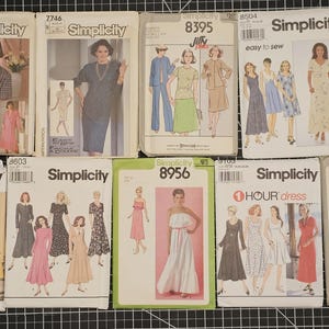May include: A collection of vintage Simplicity sewing patterns. The patterns feature illustrations of dresses, suits, and other garments. The covers display the Simplicity logo and pattern numbers, with models showcasing the finished designs.
