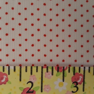 Op de afbeelding: Witte stof met een rood stippenpatroon. Een liniaal met bloemmotieven is onderaan de afbeelding geplaatst. De liniaal toont metingen van 1 tot 4 inch.