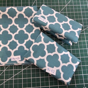 May include: Three pieces of teal fabric with a white geometric pattern. The fabric is folded and labeled with the measurements 13x42 inches, 18x21 inches, and 9x42 inches.