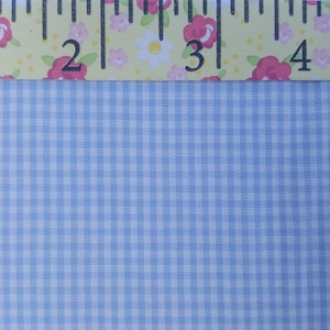 K&ouml;nnte beinhalten: Nahaufnahme eines hellblauen Gingham-Stoffes mit einem wei&szlig;en Gittermuster. Oben im Bild ist ein Lineal mit floralen Akzenten zu sehen.