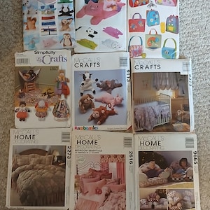 May include: A collection of nine sewing pattern envelopes from Butterick, Simplicity, and McCall's. The envelopes feature illustrations and photographs of various craft projects, including stuffed animals, children's bags, nursery bedding, and bedroom decor.