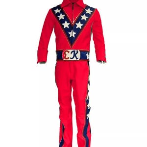 May include: A red jumpsuit with a zip-up front, collar, and long sleeves. The suit features a blue and white star design on the chest and side of the legs, with a matching belt. The belt has the letters "CK" on it.