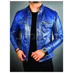 Könnte beinhalten: Blaue Jacke mit Schlangenmuster, Reißverschluss und zwei Brusttaschen mit Reißverschluss. Die Jacke wird über einem schwarzen Hemd getragen. Eine silberne Uhr und ein schwarzes Armband sind sichtbar.