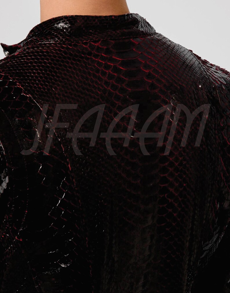 May include: A close-up of a black jacket with a red snakeskin pattern. The jacket has a high collar and a textured surface. The image shows the back of the jacket, with the word "FAAM" partially visible.