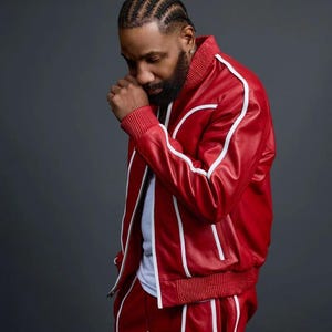 May include: Red leather track suit with white stripes. The jacket has a ribbed collar and cuffs. The pants have a drawstring waist. The outfit is worn by a person.