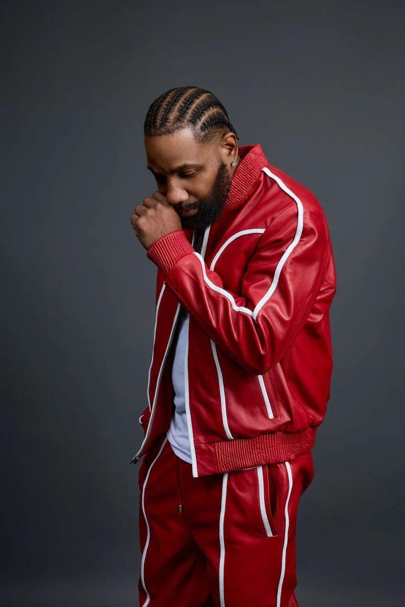May include: Red leather track suit with white stripes. The jacket has a ribbed collar and cuffs. The pants have a drawstring waist. The outfit is worn by a person.