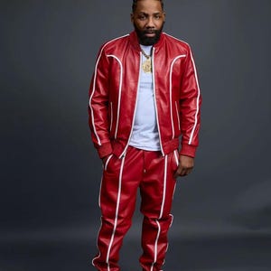May include: A red leather tracksuit with white trim. The jacket has a zipper closure and ribbed cuffs and hem. The matching pants have a straight leg design. The outfit is paired with white sneakers. The person is wearing a gold chain.