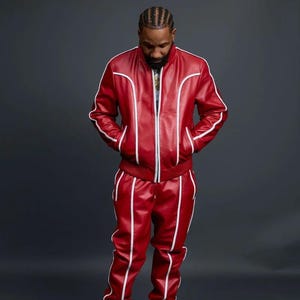 May include: Red leather tracksuit with white piping details. The jacket has a zip closure and the pants have a matching design. The outfit is paired with white sneakers. The tracksuit is a bold fashion statement.
