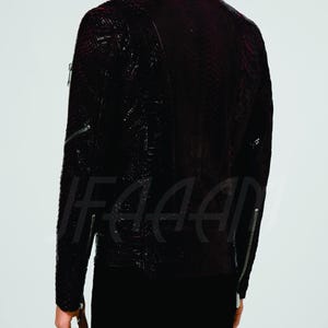 May include: A dark burgundy leather jacket with a textured pattern and silver zips. The jacket has a classic biker style with a high collar and long sleeves. The back view shows the jacket's details, including the zip pockets and seams.