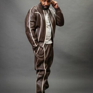 May include: A brown leather jacket and matching pants set with white piping. The jacket is a bomber style with a zipper closure. The pants have a relaxed fit. The outfit is paired with white sneakers. The person is wearing a white t-shirt.