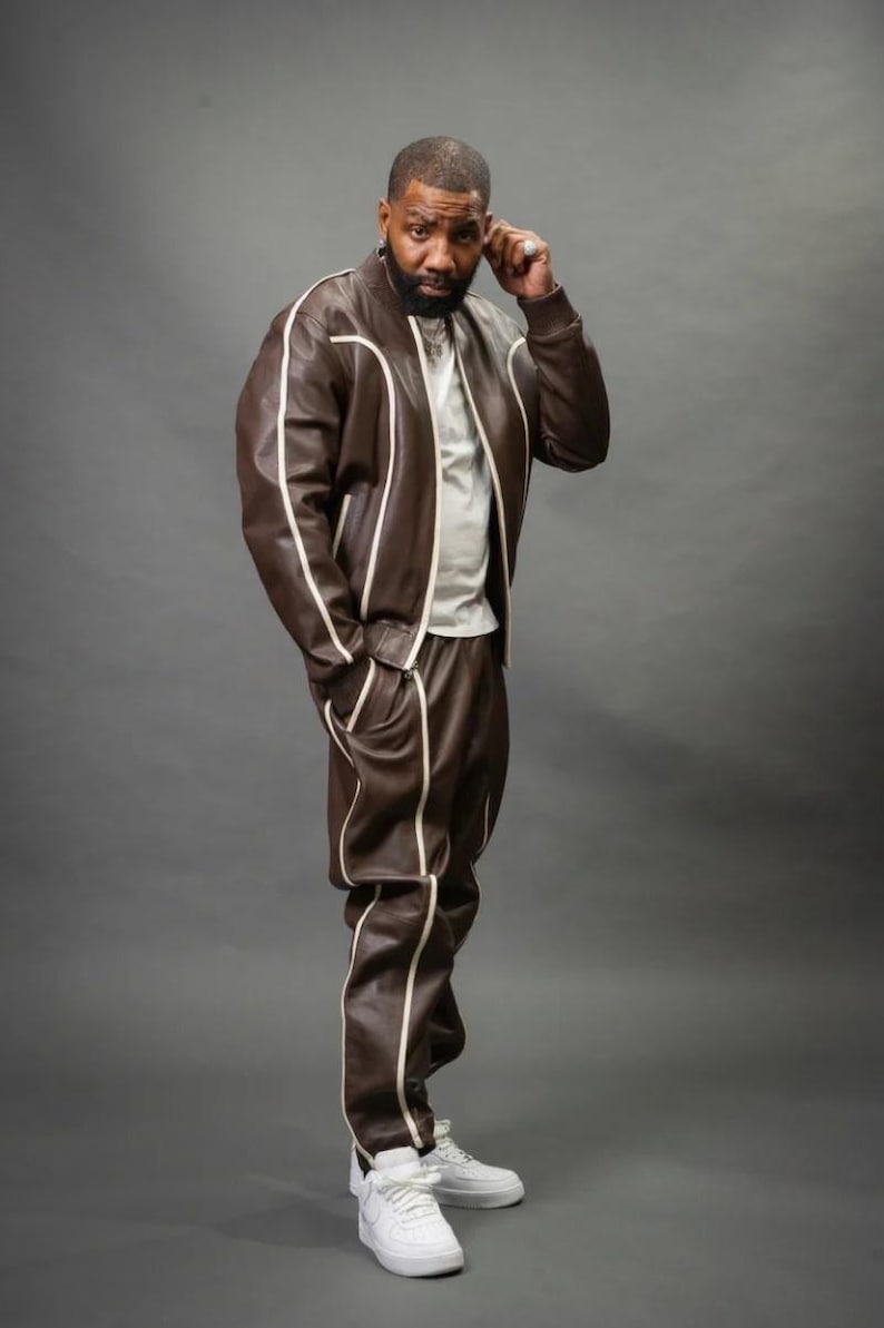 May include: A brown leather jacket and matching pants set with white piping. The jacket is a bomber style with a zipper closure. The pants have a relaxed fit. The outfit is paired with white sneakers. The person is wearing a white t-shirt.