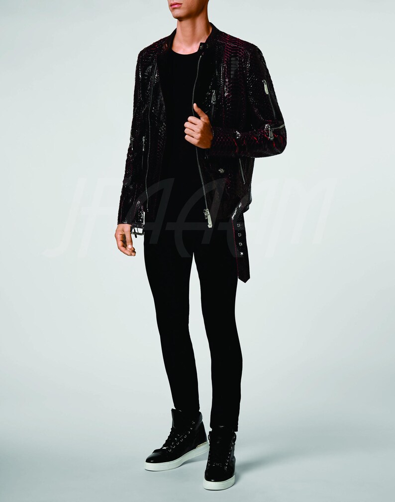 May include: A black leather jacket with a red snakeskin pattern, featuring multiple silver zippers and a belt. The jacket is paired with black trousers and high-top trainers with white soles.