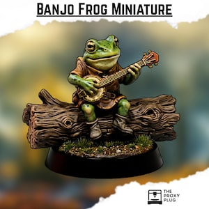 Può includere: Statuetta in miniatura di una rana verde che suona il banjo seduta su un tronco marrone. La rana indossa una tunica e stivali marroni. La base è nera con piccoli ciuffi di erba verde. Il testo "BANJO FROG MINIATURE" è in alto.