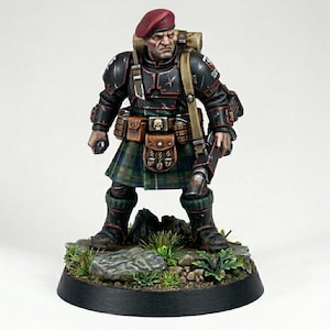 Op de afbeelding: Miniatuurfiguur van een soldaat in een rode baret en een traditionele Schotse kilt. De figuur draagt zwarte bepantsering met bruine leren zakjes en een rugzak. De basis heeft kleine rotsen en groen gebladerte.