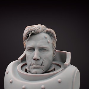 May include: A grey bust of a man with short, styled hair and a stern expression. The bust features a detailed face with visible cracks and rivets on the armor-like structure around the neck and shoulders. The sculpture has a weathered appearance.