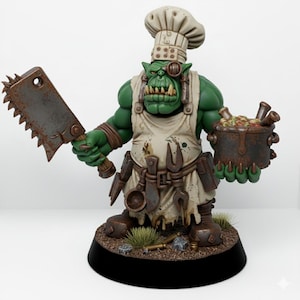 Op de afbeelding: Een groene orkfiguur met een koksmuts en schort, met een roestige vleesbijl en een pot met eten. De ork heeft een monocle en gereedschap dat aan zijn schort hangt. Het beeldje staat op een zwarte basis met gras.