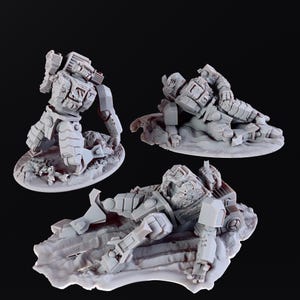 Könnte beinhalten: Drei graue Miniatur-Roboterfiguren in verschiedenen Posen, jeweils auf einer strukturierten Basis. Einer kniet, ein anderer liegt und der dritte liegt flach, was eine Kampfszene oder ein Diorama suggeriert.
