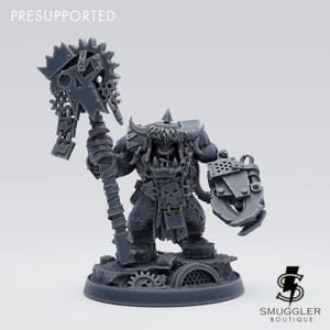 Könnte beinhalten: Graue Miniaturfigur eines Ork-Kriegers, der eine große, stachelige Waffe und einen schildartigen Greifer hält. Die Figur steht auf einer kreisförmigen Basis mit mechanischen Details. Das Wort "PRESUPPORTED" steht oben.