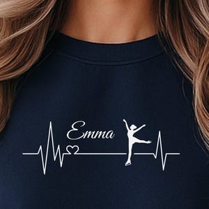 Könnte beinhalten: Marineblaues Sweatshirt mit weißer Grafik. Die Grafik zeigt den Namen "Emma" über einer Herzschlaglinie, einem Herzsymbol und einer Silhouette einer Balletttänzerin. Das Sweatshirt hat einen Rundhalsausschnitt.
