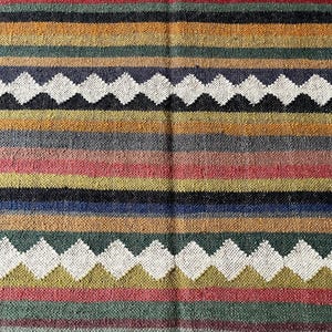 May include: A woven textile with a striped pattern in various colors, including blue, green, red, yellow, and white. The design features horizontal stripes and diamond-shaped patterns. The textile appears to be made of a natural fiber.