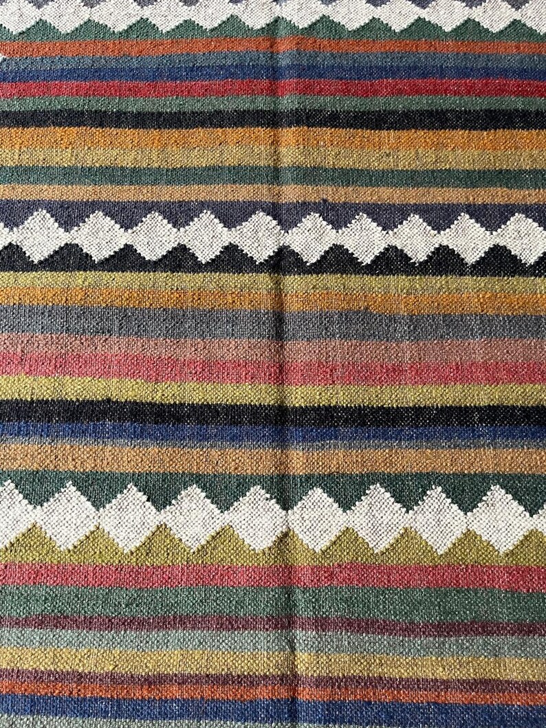 May include: A woven textile with a striped pattern in various colors, including blue, green, red, yellow, and white. The design features horizontal stripes and diamond-shaped patterns. The textile appears to be made of a natural fiber.