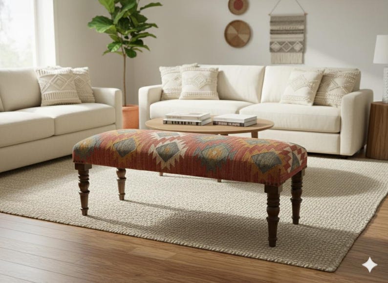 May include: A rectangular bench with a patterned fabric top in shades of red, orange, yellow, and gray. The bench has dark brown, turned legs and is placed on a neutral-colored rug in a living room setting.